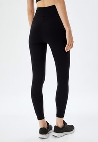 Zwarte high-waisted leggings van een gladde, rekbare stof met een aansluitend ontwerp. Gecombineerd met zwarte sport schoenen.