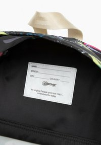 Vícebarevná vnitřnost tašky Eastpak, která ukazuje černou podšívku a bílou nálepku s polem pro jméno, ulici, město a zemi.