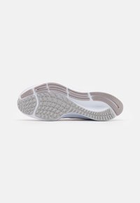 Suela de zapatilla deportiva blanca con patrones de tracción de goma marrón claro y ranuras para flexibilidad, que presenta una superficie texturizada en gris.