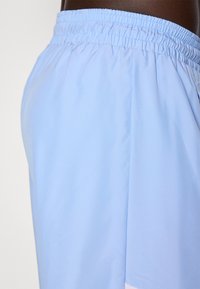 Lyseblå atletiske shorts lavet af glat, let stof. Har en elastisk talje og sidelommer for nemhed.