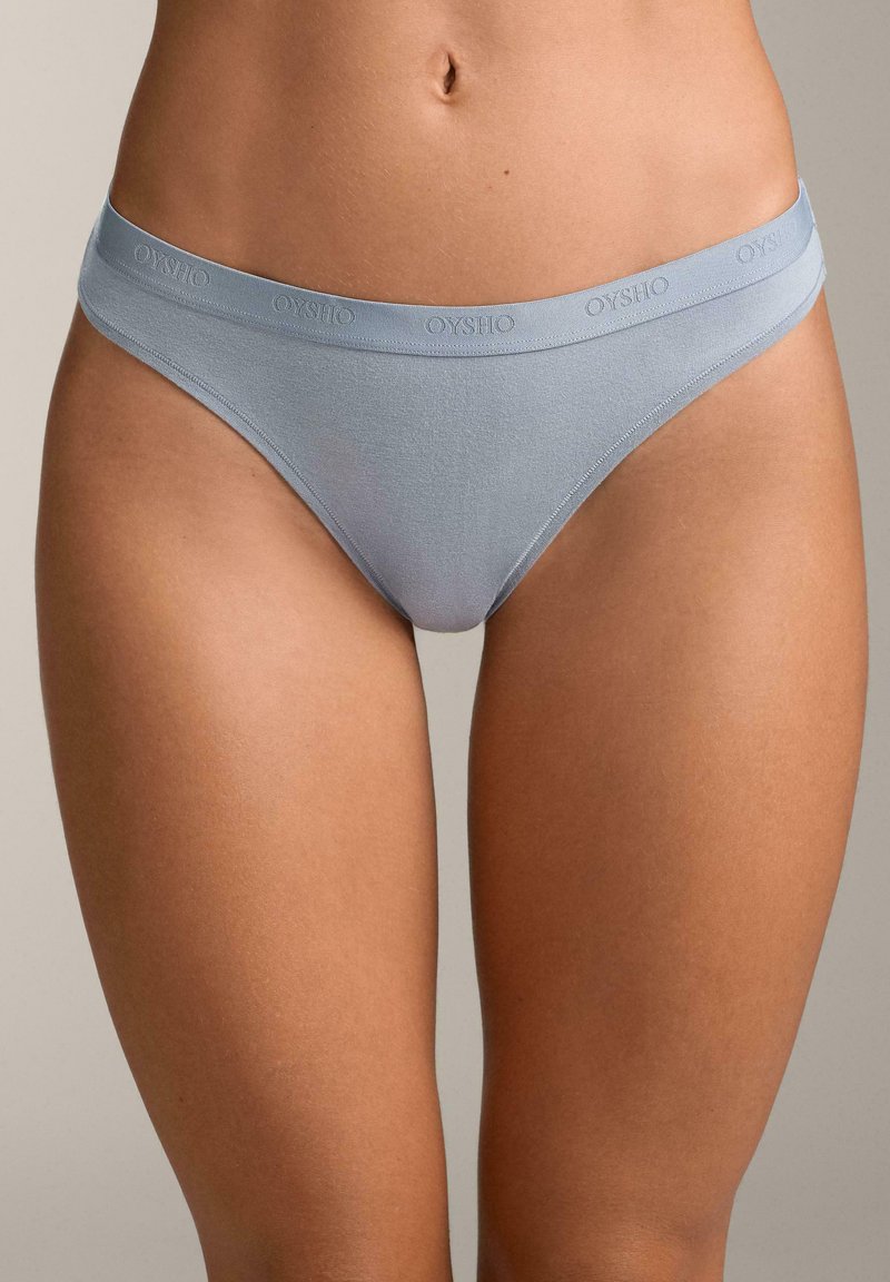 Lichtblauwe katoenen string met een gladde textuur, voorzien van een elastische tailleband waarop de merknaam "OYSHO" lichtjes is gereflecteerd.