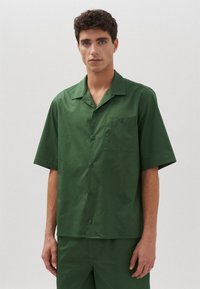 Camicetta verde a maniche corte con bottoni, realizzata in tessuto morbido, dotata di taschino sul petto, colletto a punte e vestibilità rilassata.