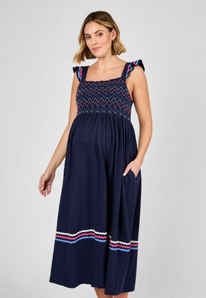 Vestido de maternidad azul marino con tirantes con volantes, smocking texturizado en el cuerpo y acentos de rayas onduladas en rosa, azul y crema en el dobladillo.