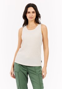 Top in tessuto a coste beige senza maniche con scollatura rotonda, abbinato a pantaloni cargo verdi con tasche laterali e cuciture in evidenza.