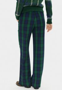 Pantaloni flared a quadri verdi e blu navy realizzati in un tessuto morbido, con vita alta e una consistenza liscia. Presentano cuciture laterali sottili.