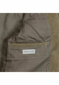 Grauer Stoff mit einem Wildleder-Akzent; besitzt ein aufgenähtes Etikett mit der Aufschrift "Bis dass der Tod uns scheidet." Glatte Textur mit einfachem Taschen-Design.