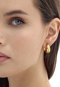 Goldene Creolen mit einem glatten, halb verdrehten Design. Die Ohrringe sind poliert und reflektieren das Licht, was ihr glänzendes Aussehen unterstreicht.