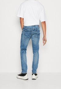 Vaqueros de denim azul claro con corte ajustado, cinco bolsillos y una textura desgastada. Combinados con una camiseta blanca y zapatillas negras y blancas.