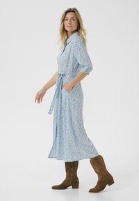 Ljusblommig klänning med trekvartslånga ärmar, midjebälte och fickor. Kombinerad med bruna mocka knähöga stövlar.