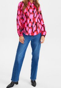Blusa a maniche lunghe a righe rosa e rossa con colletto, abbinata a jeans blu dritti e stivali con tacco neri alla caviglia.