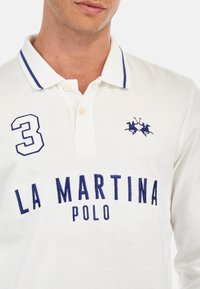 Bílá polo košile vyrobená z bavlny, s modrými vyšívanými detailem, včetně čísla "3" a textu "LA MARTINA POLO", a dvoubotonovým límečkem.