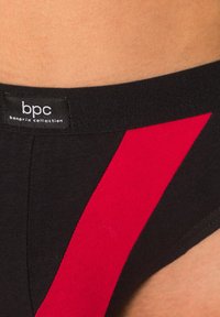 Slip in cotone nero con una ampia striscia rossa e una vita elastica con etichetta "bpc bonprix collection". Texture liscia e design aderente.