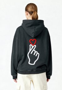 Felpa nera con un grande design ricamato di una mano che forma un cuore con le dita, contornato di bianco e accentuato da un cuore rosso.