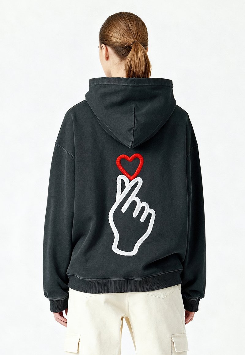 Felpa nera con un grande design ricamato di una mano che forma un cuore con le dita, contornato di bianco e accentuato da un cuore rosso.