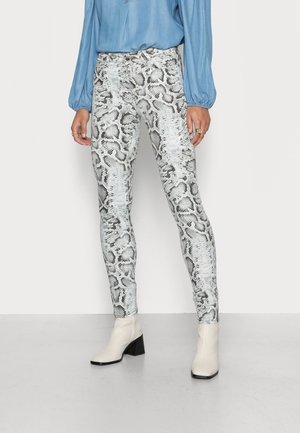 Calças justas com padrão de serpente em preto e branco, apresentando um padrão texturizado. Combinadas com uma blusa azul-clara e botas brancas até o tornozelo.