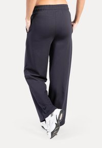 Marineblauwe sweatpants met een losse pasvorm, elastische tailleband en zijzakken. Gedragen met witte sportschoenen met grijze accenten.