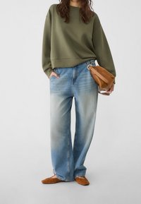 Olijfgroen sweatshirt, losse fit; blauwe denim jeans met een lichte wassing; bruine suede flats; beige clutchtas met een hengsel.
