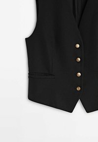 Gilet noir sur mesure avec quatre boutons dorés et une petite poche sur le côté gauche sur fond blanc.