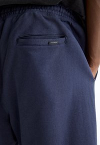 Shorts bleu marine en mélange de coton avec une taille élastique et une poche arrière unique. Présente une étiquette discrète "PULL&BEAR" sur la poche.