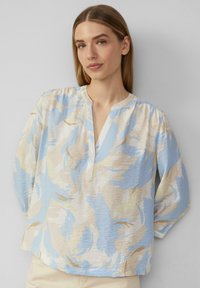 Lichte blouse met een pastelbloemenpatroon in blauw en beige, voorzien van een V-hals en driekwart mouwen. Geweven stof.