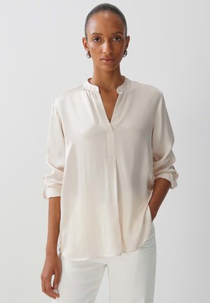 Light beige, long-sleeve blouse with a mandarin collar, soft texture, elbow-length sleeves rolled up, and a relaxed fit.