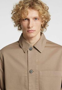 Beige bomullsskjorte med spiss krage, knappelukking foran og en brystlomme med strukturert stoff.