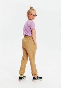 Uformel påklædning bestående af en lavendel t-shirt og lysebrune bukser med elastisk talje. Sorte sneakers med hvide såler, hår i en knold.