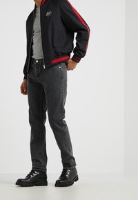 Black bomber jacket with red stripes, gray t-shirt, dark gray jeans, and black boots with silver eyelets. Casual urban outfit.