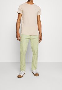 Light beige T-shirt with a round neckline, paired with light green pants. White sneakers with brown soles complete the look.