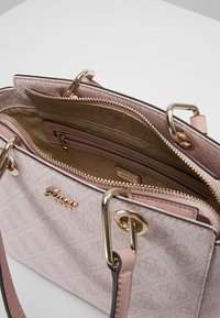 Vaaleanpunainen kuviolaukku, jossa on kultaiset yksityiskohdat ja vetoketjukiinnitys. Sisätilassa on useita lokeroita ja sileä pinta.