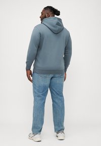 Sweat-shirt à capuche en tissu bleu doux, avec une poche kangourou et un ourlet côtelé. Assorti à un jean droit bleu clair et des baskets.