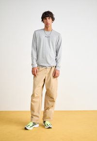 Ljusgrå långärmad skjorta, beige cargobyxor och sneakers med neongröna accenter. Rena linjer och enkel design med metalldetalj i halsbandet.