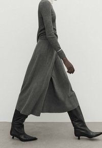 Grå ulltröja i kombination med en lång grå kjol och svarta spetsiga stövlar; slank silhuett med en strukturerad yta.