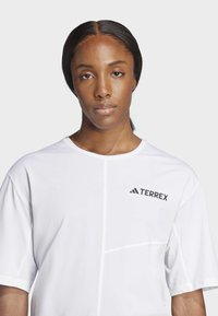 Bílá krátký rukáv tričko s kulatým výstřihem, s černým logem "TERREX" a elegantním švem pro moderní sportovní vzhled.