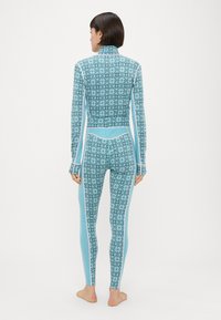 Ολόσωμο μαγιό σε ανοιχτό μπλε με γεωμετρικό σχέδιο. Διαθέτει ψηλό γιακά, μακριά μανίκια και λωρίδες στα πλευρά σε αντίθετο χρώμα.