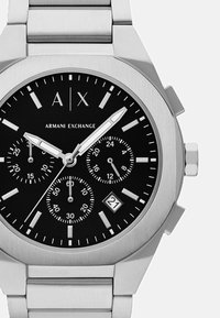 Orologio cronografo in acciaio inossidabile con quadrante nero, indici delle ore in argento, display della data e logo distintivo. Dotato di bracciale a maglie in metallo.