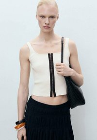 Rebrasti kremasti crop top s kvadratnim izrezom i smešastim naglaskom; uparen s crnom suknjom i tkanom crnom torbicom.