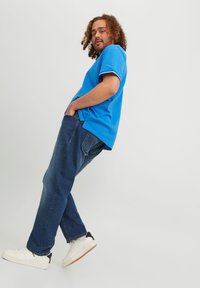Camisa polo de manga corta azul con detalles en blanco, combinada con vaqueros oscuros y zapatillas blancas de caña baja, con un ajuste holgado.