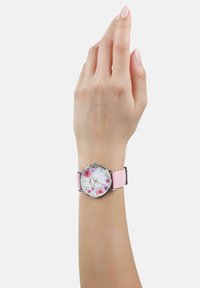 Kwarts horloge met een witte wijzerplaat met roze bloemenpatronen, zilveren uurmarkeringen en een lichtroze siliconen band.