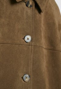 Close-up of brown suede coat front with dark brown, four-hole buttons and visible vertical and horizontal stitching details.
