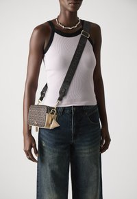 Sacoche à bandoulière brun à motifs avec des accessoires en or et une sangle noire. Portée avec un débardeur léger et un jean bleu ample, illustrant un style décontracté.
