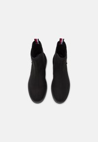 Botas de tobillo de ante negro con una textura suave, punta redondeada y paneles laterales elásticos. Presentan una tira de tirador a rayas en rojo, blanco y azul.
