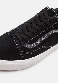 Baskets en daim noir avec lacets noirs, surpiqûres blanches et semelle en caoutchouc blanche. Présente un motif latéral signature en surpiqûres grises.