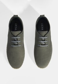 Chaussures perforées vertes avec lacets gris, dotées d'une tige lisse et d'une semelle à motifs pour une meilleure adhérence. Deux tirettes à l'arrière.