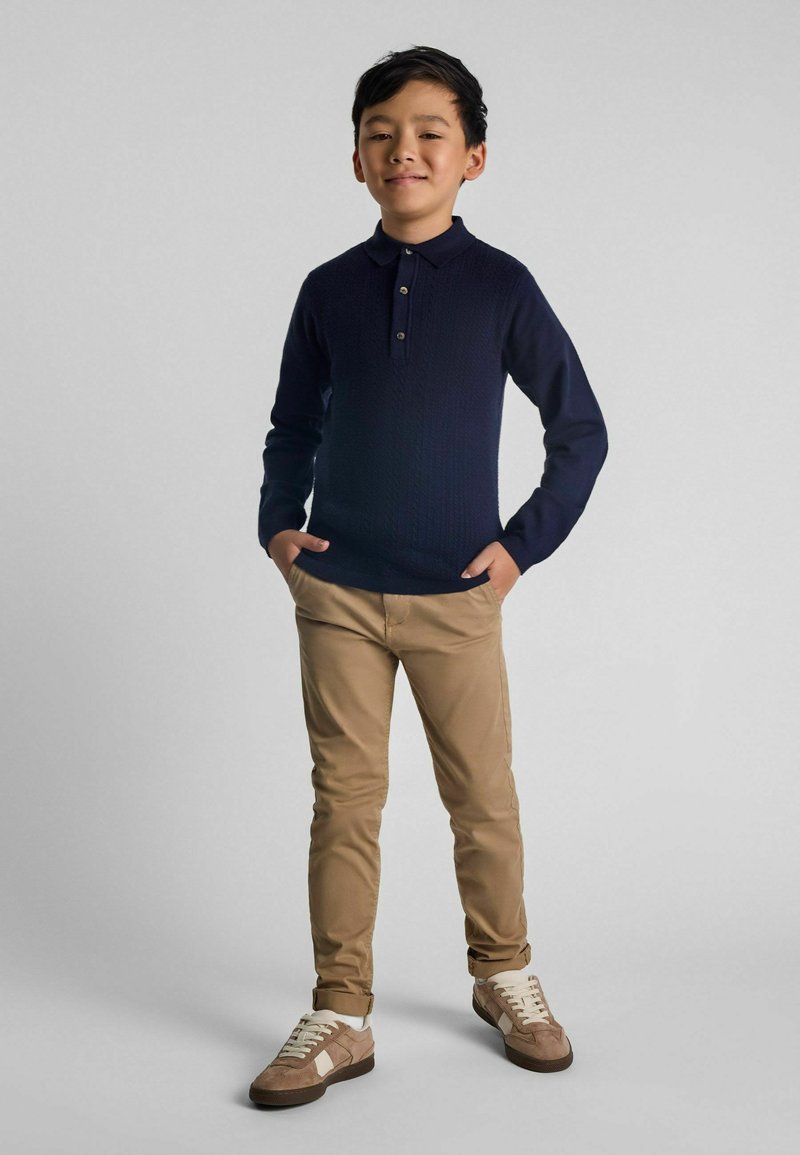 Polo de punto azul marino con cuello y tres botones, combinado con chinos beige claros y zapatillas marrones con detalles en blanco.