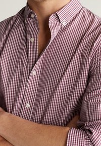 Camisa de cuadros rojos y blancos con textura suave, cuello abierto y mangas largas, con botones blancos y puños contrastantes.