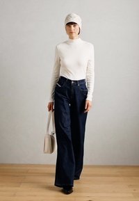 Hvid langærmet top parret med højtaljede, vide mørke denim jeans. En lysfarvet mønstret strikhue og en lille hvid håndtaske fuldender udseendet.