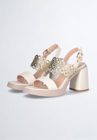 Witte gehakte sandalen met een chunky blokhak. Heeft een brede band met ronde uitsparingen en metallic accenten, die is vastgezet met een gesp.