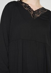 Vestido preto de manga longa com decote em V de renda, apresentando tecido franzido na cintura para uma silhueta fluida e material texturizado.