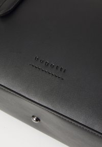 Zwarte leren tas met subtiele textuur, voorzien van de geperste "bugatti" branding en een gestikte accent. Zichtbaar detail in zilveren hardware.